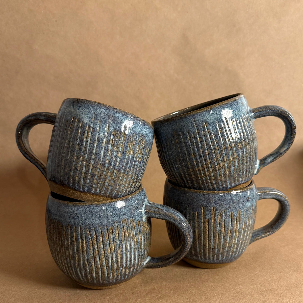 Four dark gray ceramic mugs with textured design on a brown background